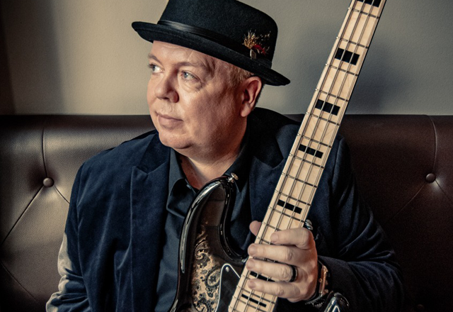 Musiker Günter Asbeck im Portrait mit Bass in der Hand auf der Couch
